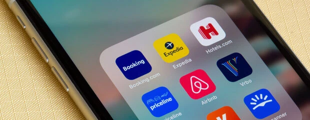 Captura de tela de artigo sobre tráfego pago versus OTAs, exibindo a tela de um smartphone com ícones de aplicativos de viagem como Booking, Expedia e Airbnb.